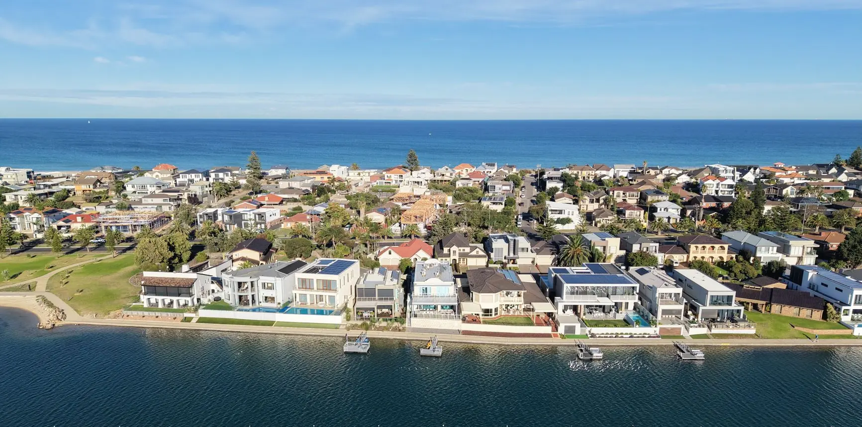 Aerial view of an Australian coastal suburb at first light, gum trees between brick and weatherboard houses with the ocean on the horizon