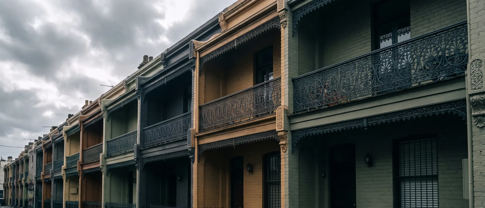 A row of Victorian terrace houses in inner Melbourne with cast iron balconies under flat silver southern light